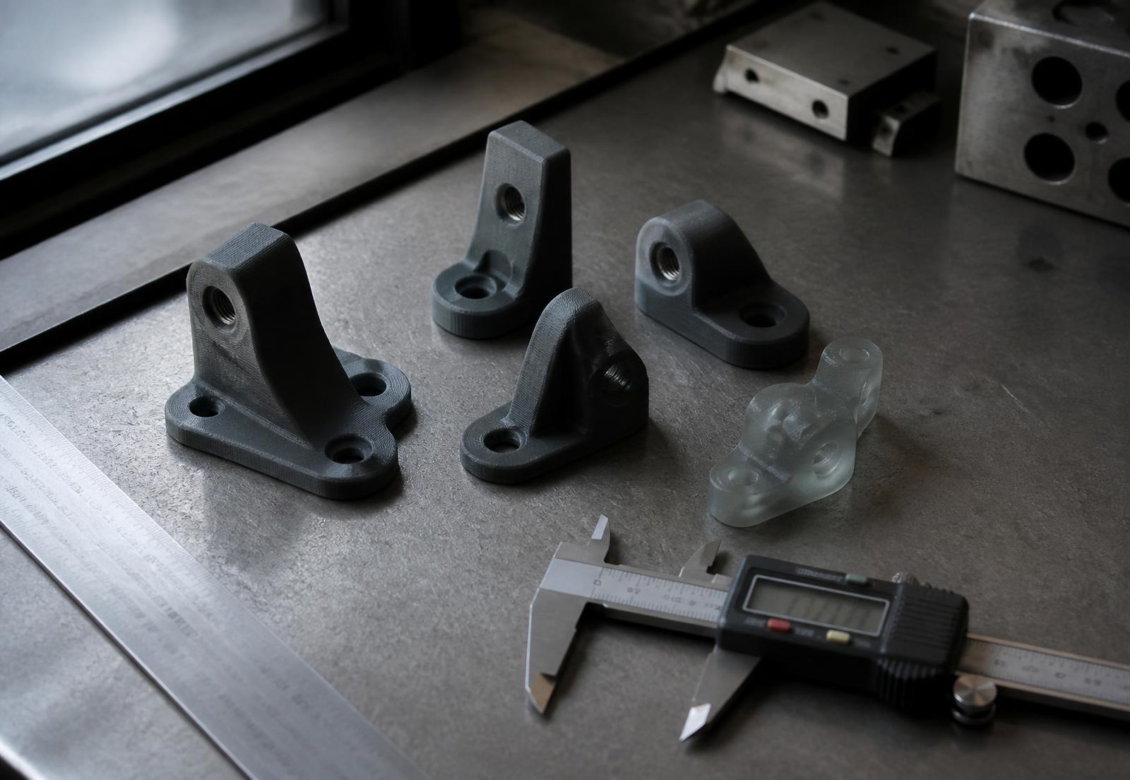 Batch of FDM and SLA printed parts measured with a digital caliper on a workshop bench